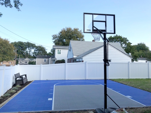 Bright blue and gray basketball half court in a fenced backyard