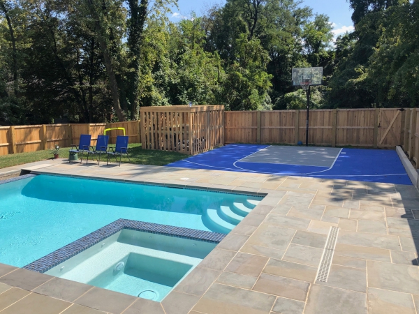 Blue and gray basketball court in a backyard with a pool