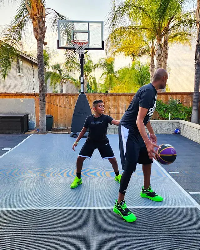 A father and son play basketball on their small backyard basketball court