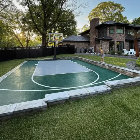 A boy plays basketball on his Dunkstar court after a rain storm. The Dunkstar court is Evergreen with a gray key and white lines.