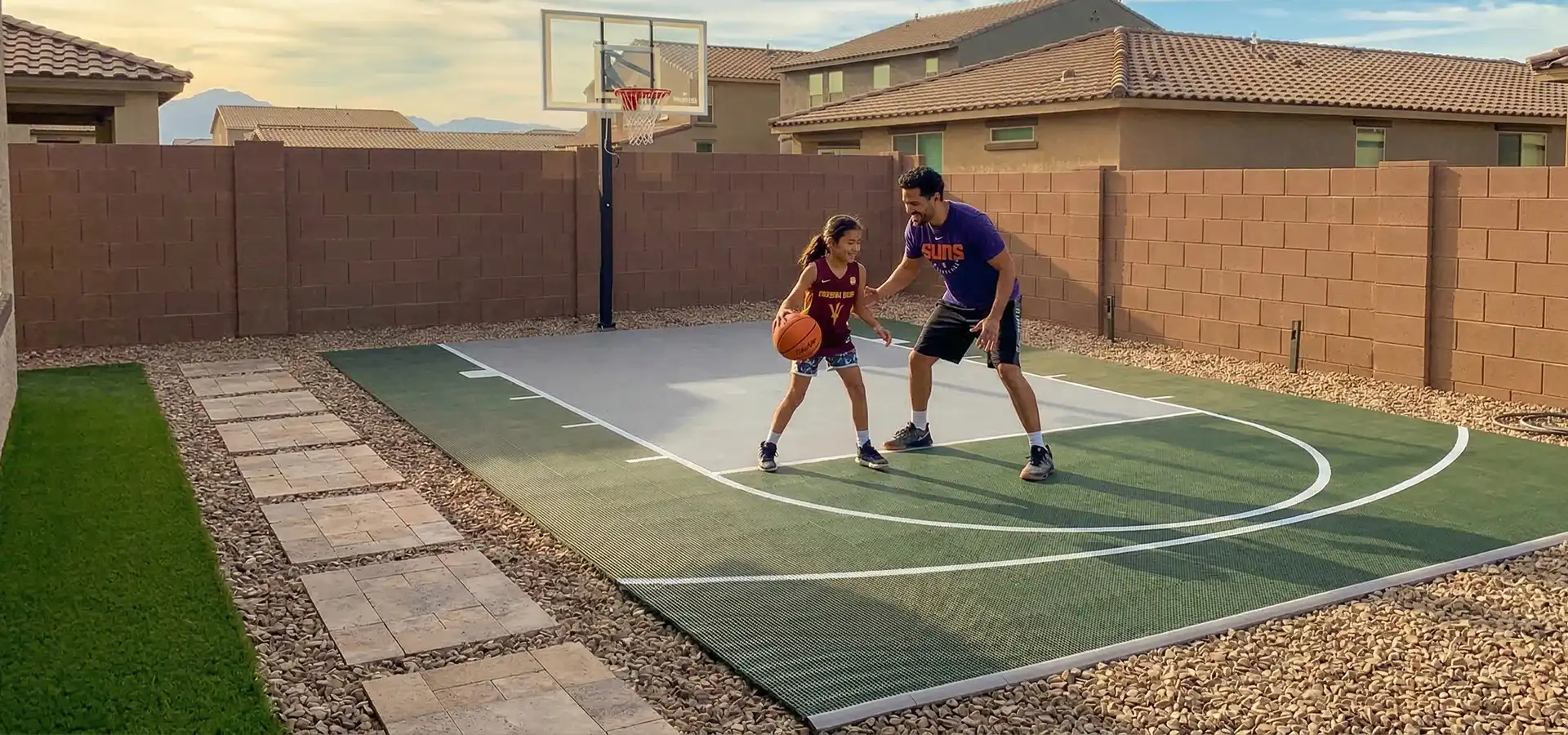 Father and daughter play a game of basketball in their backyard on a Dunkstar basketball court